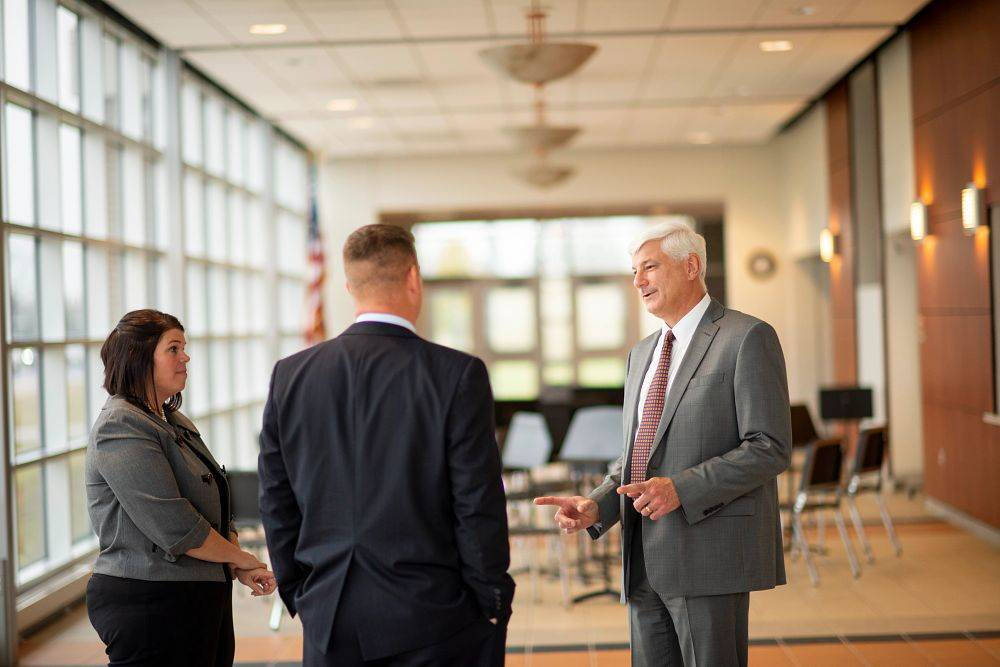 A man in a gray suit pointing while talking to two other people in business attire